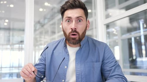 Webcam view. Amazed happy businessman looking surprised at camera or laptop screen sitting in office