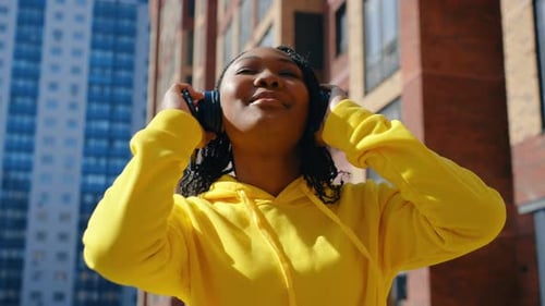 African American Woman Listening to Music with Headphones at Sunset in the City Dancing