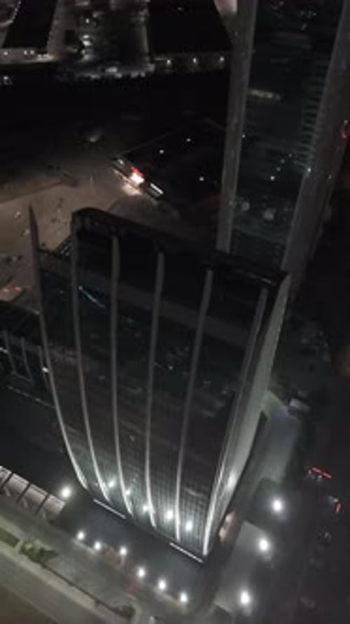 Drone flying forward passing modern buildings towers, above busy traffic road