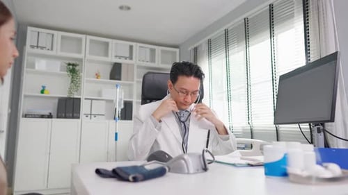 Der asiatische Kardiologe hört einer Frau mit Herzschlag im Krankenhaus zu.