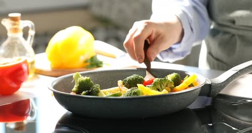 Woman cooking different vegetables in frying pan on stove indoors, closeup