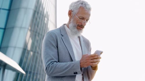 Senior Man Checks His Phone Outside Office Building