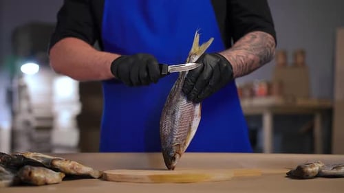 Unbekannter tätowierter Koch schneidet in der Küche Flossen von getrocknetem Fisch ab