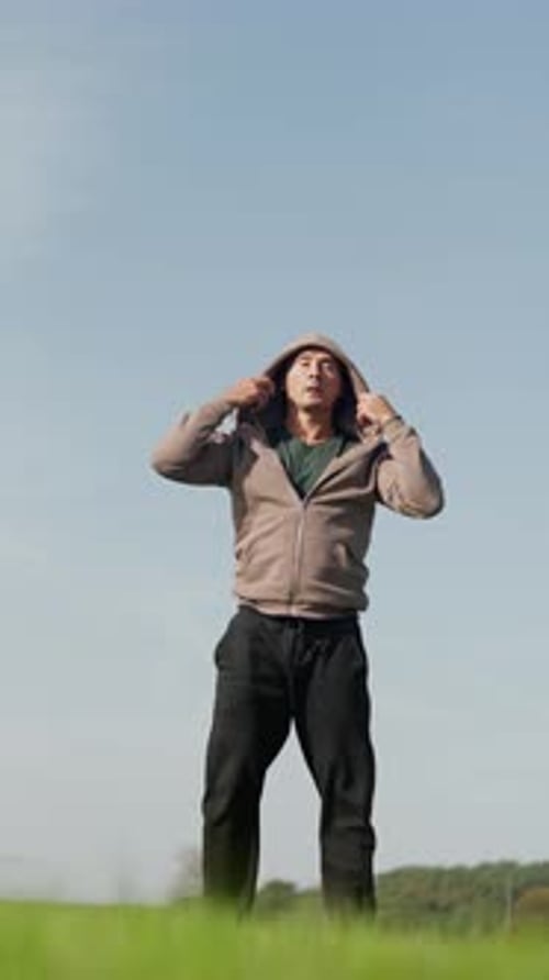 Man Puts up Hoodie on Green Grass