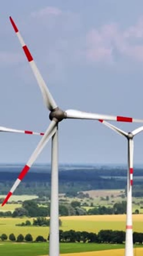 Portrait aerial view orbiting a wind power generator, sunny, summer day in Europe