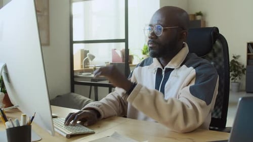 Desarrollador de software negro cansado con gafas trabajando en una computadora