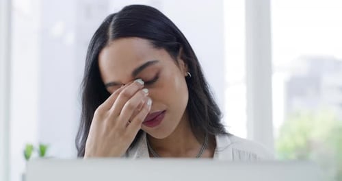 Woman Massaging Temples at Desk in Bright Office