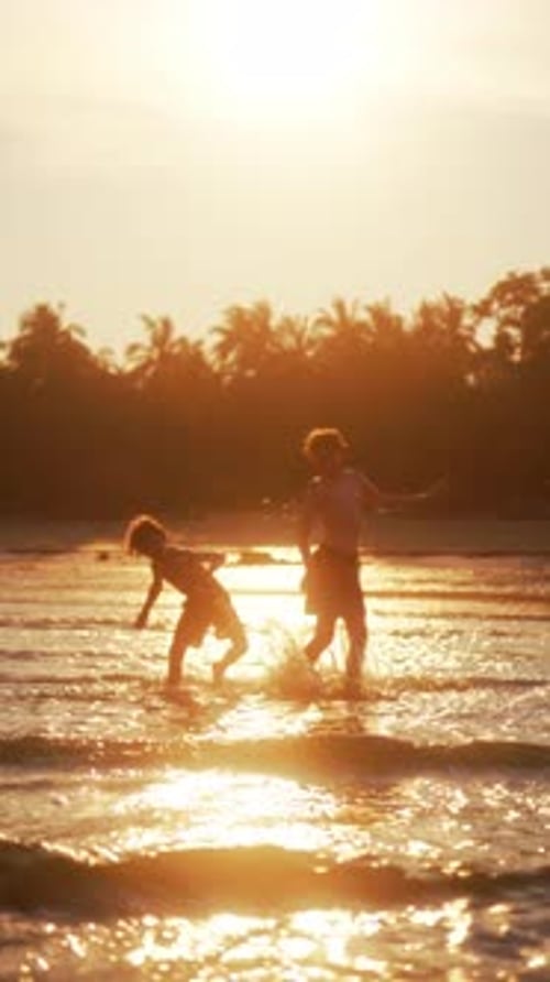 Young Boys Splashing In Shallow Ocean Waves At The Beach