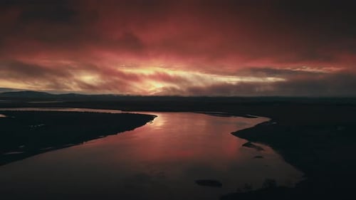 Incredibly gorgeous drone aerial of a red sunset or sunrise against a river. The camera tracks backw