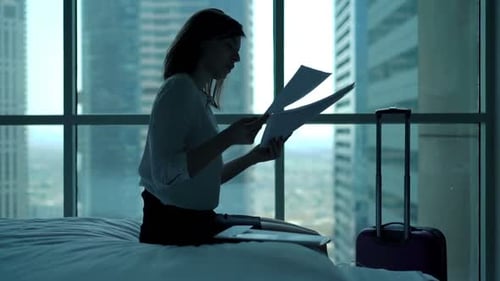 Young Businesswoman Working with Documents on Bed in Hotel Room 30s