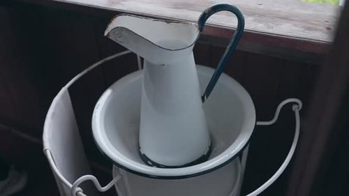 vintage white enamel pitcher resting in matching basin with metal stand