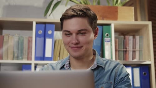 Young Man Smiling Looking at Computer in Home Office