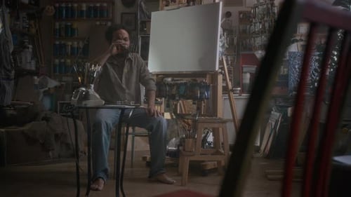 Stressed Artist Drinking Whiskey before Painting in Cluttered Workshop