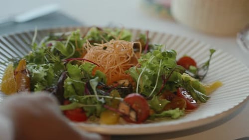 Camarero que sirve ensalada mixta con hojas verdes, tomates cherry y frutas cítricas