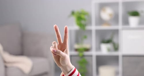 Woman showing V-sign at home, closeup view