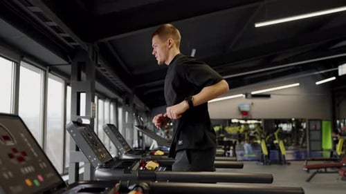 Concentrated Man Runs on Treadmill in Modern Fitness Club Enhancing Endurance