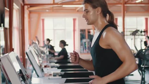 Jovem atleta caucasiano masculino com um corpo musculoso suado correndo em uma esteira em uma academia coberta
