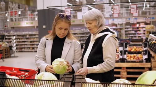 An Old Grandmother and an Adult Daughter are Buying Cabbage in a Grocery Store