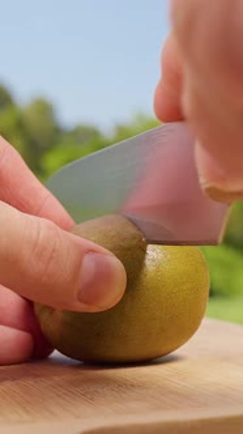 Vertical video. Hand Cutting Red Kiwi Variety on Wooden Cutting Board Outdoors in Close Up Macro