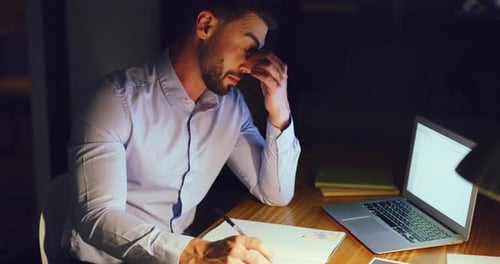 Stressed business man working late on a laptop in an office at night
