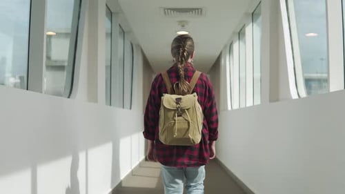 Woman with Backpack Walks Along Airport Walkway