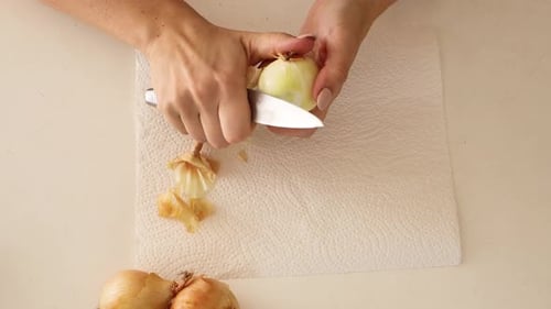 Woman Peels Onion with Knife for Cooking Preparation
