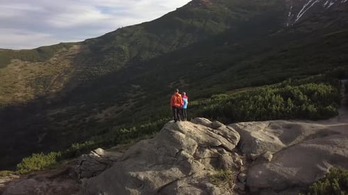 Luftbild eines Wanderers und seines Kindersohnes, die zusammen auf einem großen Felsen in den Bergen klettern