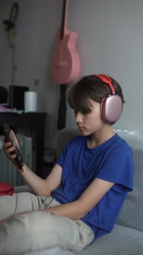 Young Person Using Phone with Headphones on Couch