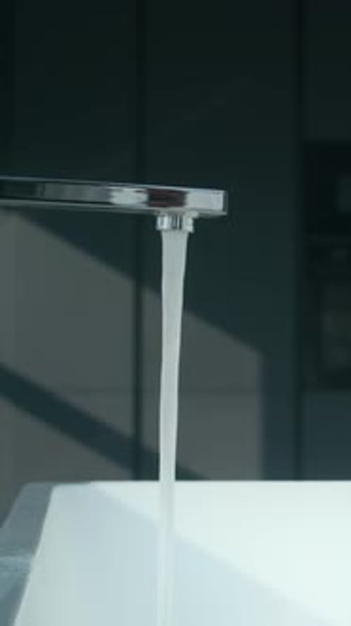 Vertical Close Up of Modern Chrome Faucet Pouring Water in Freestanding Bathtub