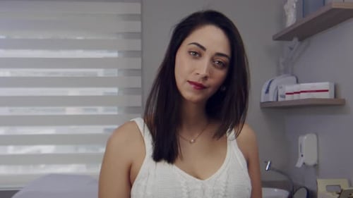 Woman in a clinic or doctors office looks and smiles up as someone enters
