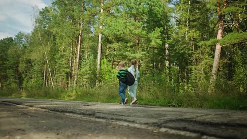 Siblings Walking Along Cracked Tar Road in Sunlit Forest