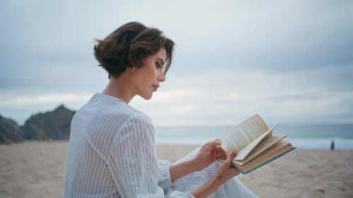 Nachdenkliche Frau mit Buch am Meer, Strand, Nahaufnahme, fokussiertes Model, blättert Seiten um