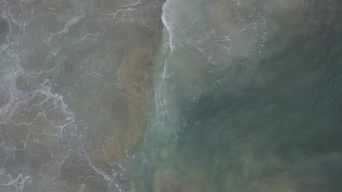 Stormy sea with waves breaking, white foam and beach sand dragged into the sea