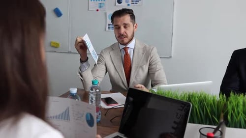 Business Negotiations in the Office Between Businessmen with Graphs and Papers with Laptops on the