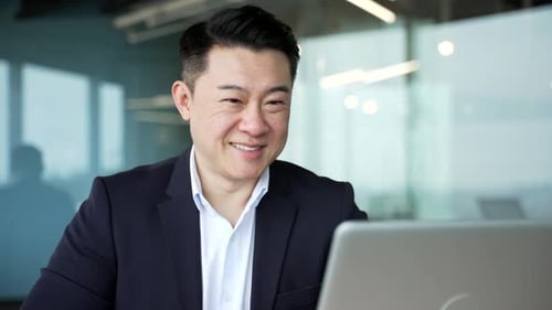 Smiling asian businessman working on a laptop sitting at workplace in business office. Male worker