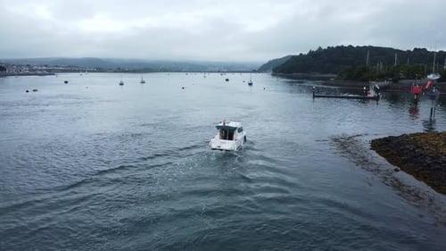 Motor boat aerial view arrives Conwy seaside town harbour estuary to navigate quiet river