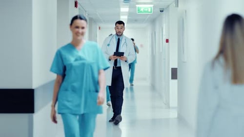 Determined Handsome Doctor Uses Digital Tablet Computer while Walking Through Hospital Hallway in S