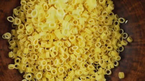 Small ring-shaped pasta is poured into a brown ceramic bowl. Top view. Slow motion.