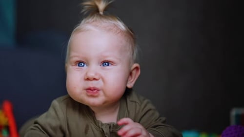 Beautiful Caucasian baby with blond hair. Cute child crawls up to a camera. Close up.