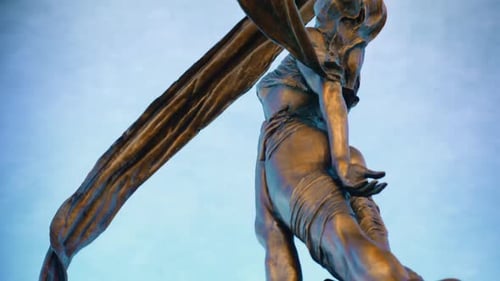 Slow pan down gimbal shot of a majestic gold statue against a striking blue sky. A gorgeous piece o