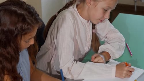 Two Little Schoolgirls Joyfully Coloring Together During Art Class