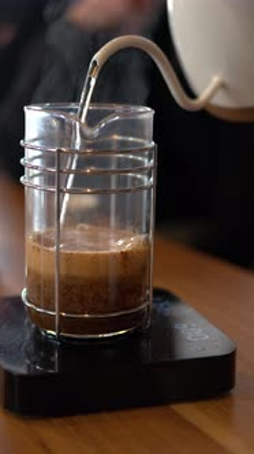 Close up of water pouring over coffee in a french press in a slow, circular motion. Vertical