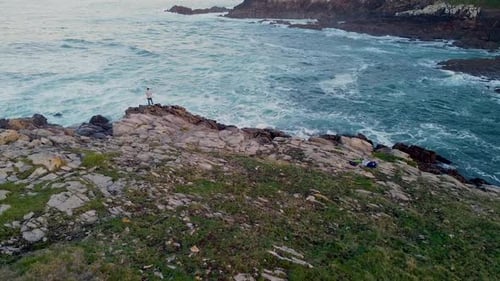 Person Standing On The Edge Of Cliffs Looking On Sea Waves Crashing On Rocks. - aerial ascend