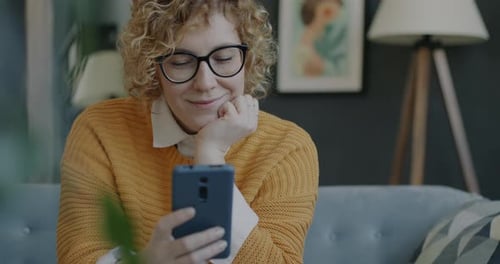 Portrait of Joyful Lady Using Smartphone Reading Messages and Laughing Indoors in Apartment