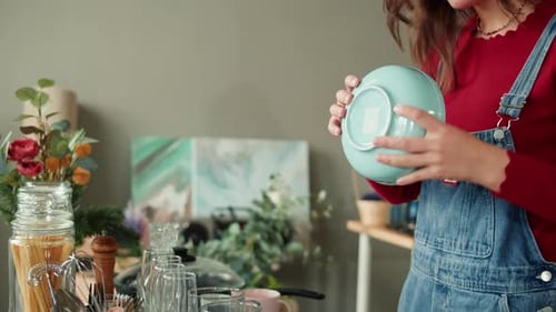 Woman Sorts Kitchenware on Table Indoors