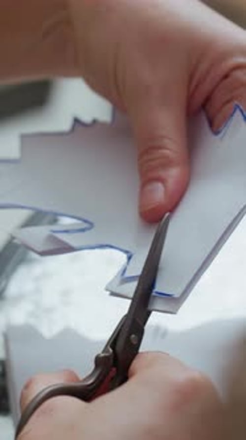 Hands Cutting Paper with Scissors on Table