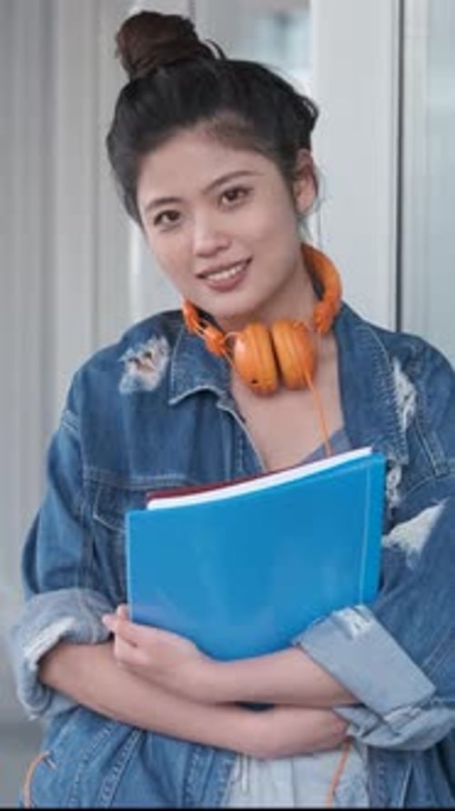 Asian College Student Holding Folders and Looking at the Camera While Standing at the Hallway