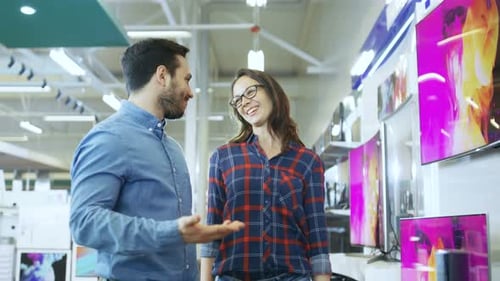 Young Couple Shopping for a New 4K TV Set in the Electronics Store. They're Trying to Decide on the