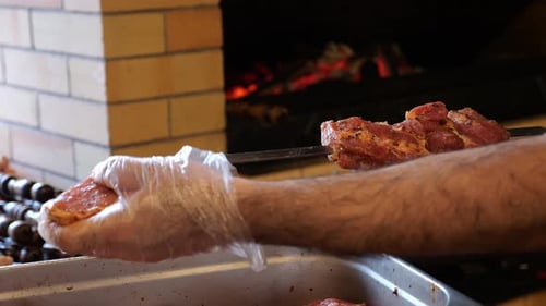 Closeup of a Chef Wearing Gloves Stringing Marinated Pork Meat on a Skewer