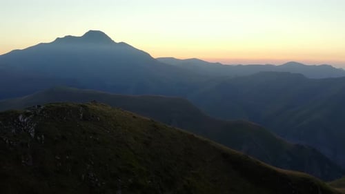 Shot of a drone, flying over the crest of a mountain with a sunset in the background.